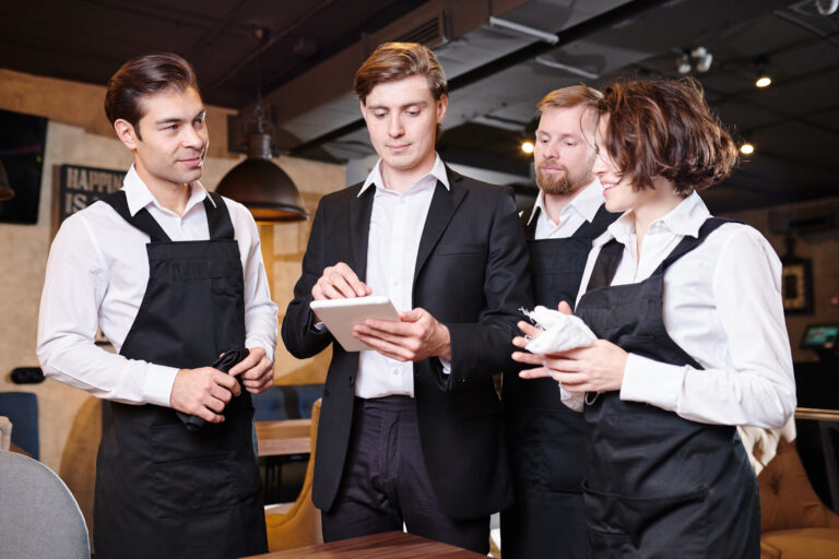 Restaurant manager discussing responsibilities with staff, utilizing tablet for inventory management.