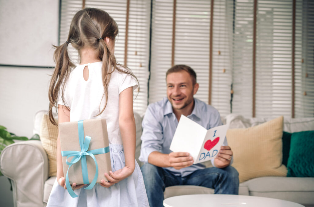 Little girl giving father a heartfelt card and wrapped gift, thoughtful gift ideas.