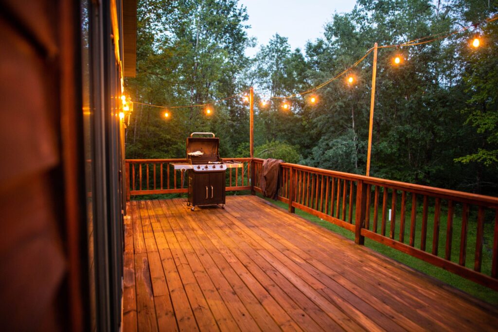 Wooden porch with string lights and grill enhancing outdoor living space