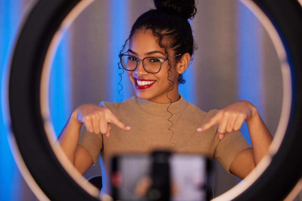 Young woman influencer with ring light and smartphone, promoting social media growth.