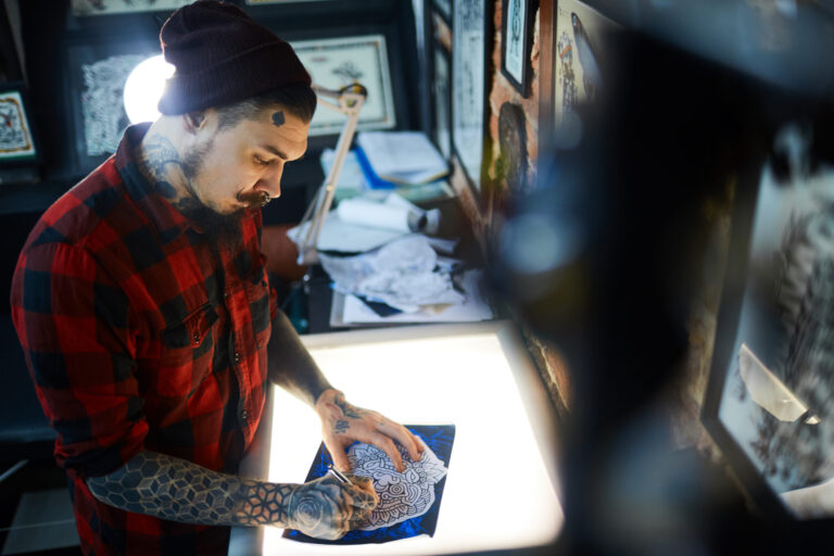 Tattoo artist sketching design on light box, preparing tattoo artwork