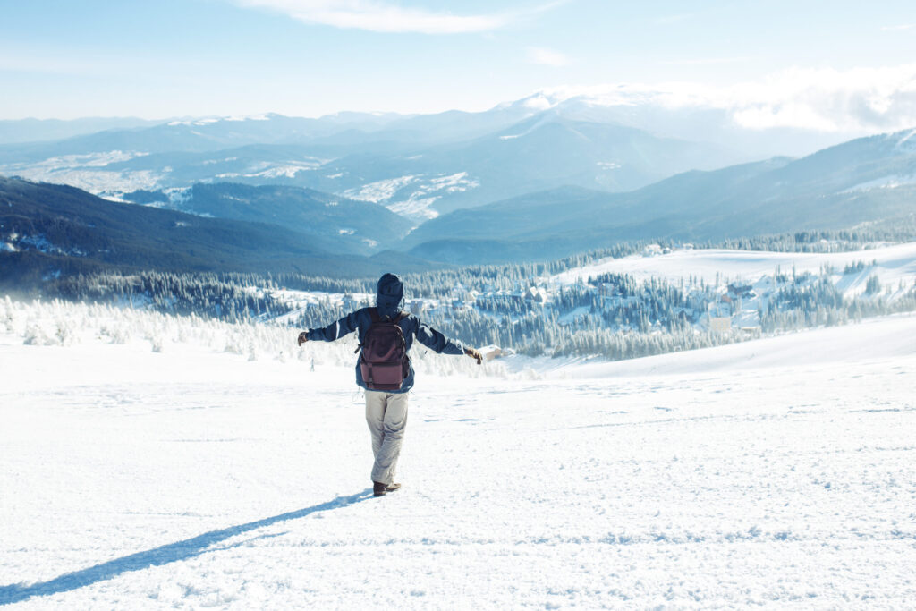 Hiker with backpack trekking in snowy mountains, cold weather safety precautions