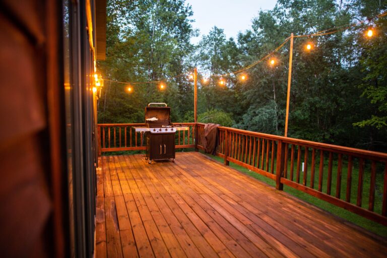 Wooden porch with string lights and grill enhancing outdoor living space