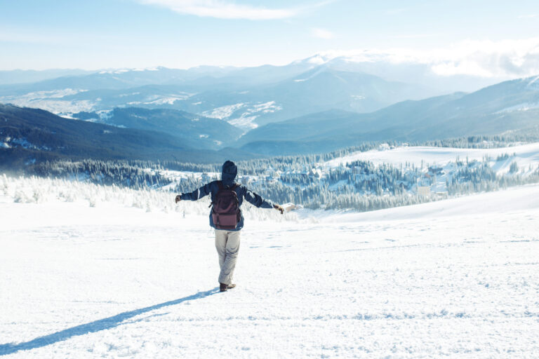 Hiker with backpack trekking in snowy mountains, cold weather travel destination.