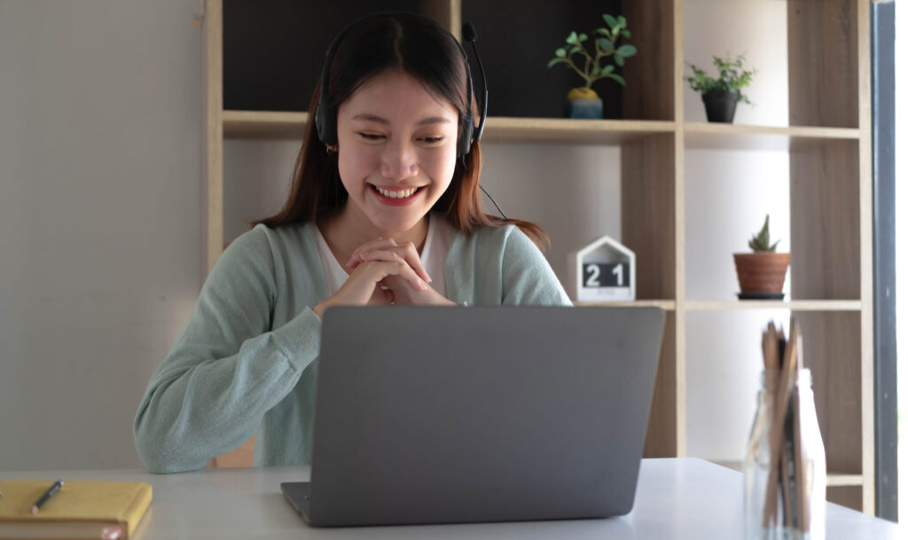 Asian student smiling and using laptop for online search and community connection.